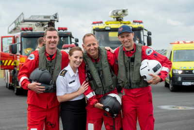 A woman in Navy uniform with three helicopter crew members in front of emergency service vehicles