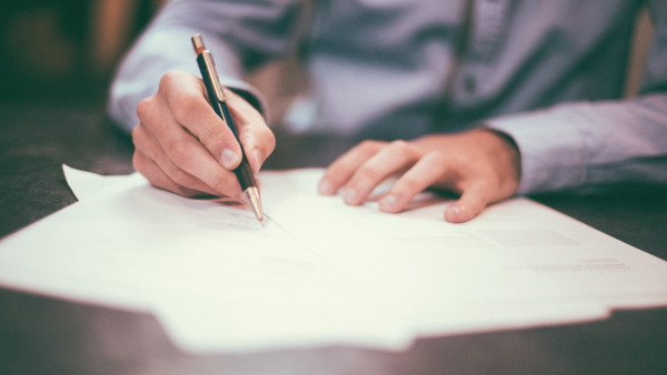 A man signing a stack of papers on a table.